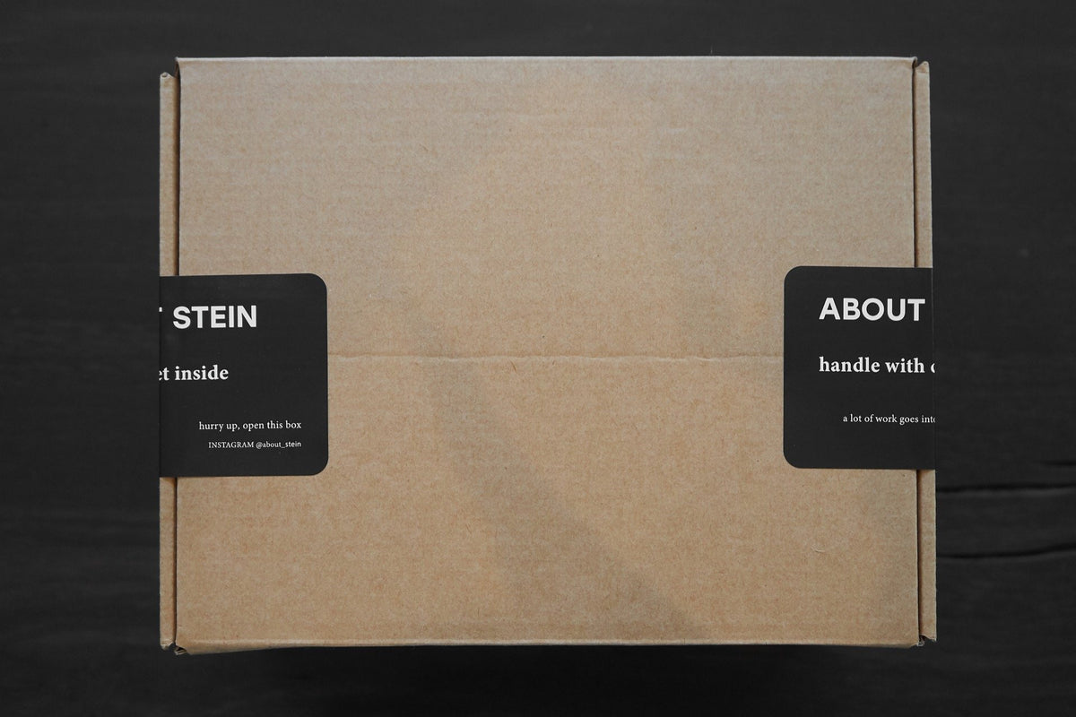 Karton, der an den Seiten mit einem schwarzen Aufkleber von About Stein zugeklebt ist