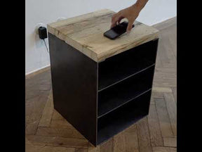 Nachttisch aus rohem Stahl, drei Fächern und einer Platte aus Altholz Fichte, auf der ein Handy liegend induktiv auflädt