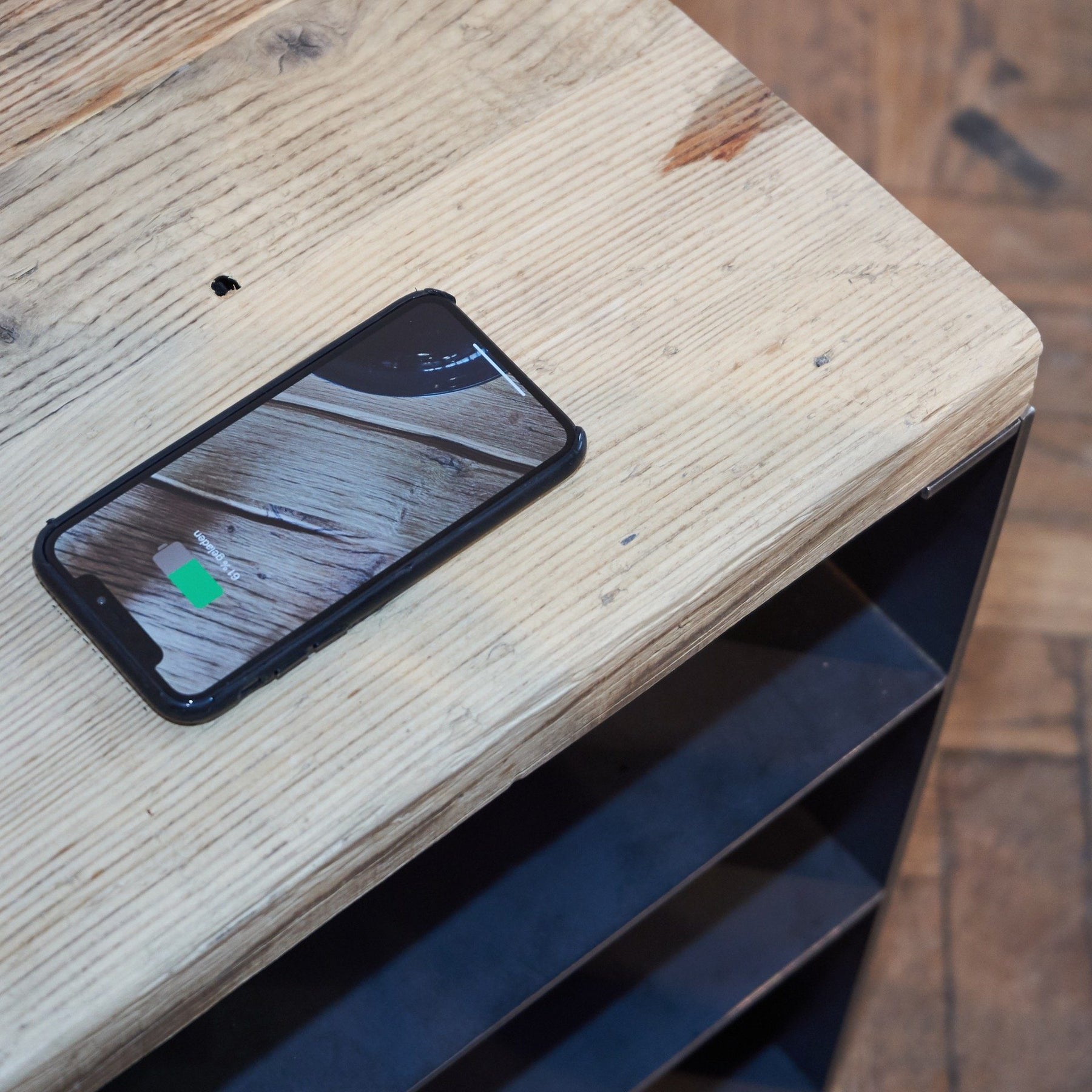 Nachttisch aus rohem Stahl, drei Fächern und einer Platte aus Altholz Fichte, auf der ein Handy liegt, das induktiv auflädt