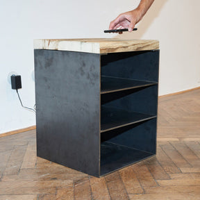 Nachttisch aus rohem Stahl, drei Fächern und einer Platte aus Altholz Fichte, auf die eine Person ein Handy legt