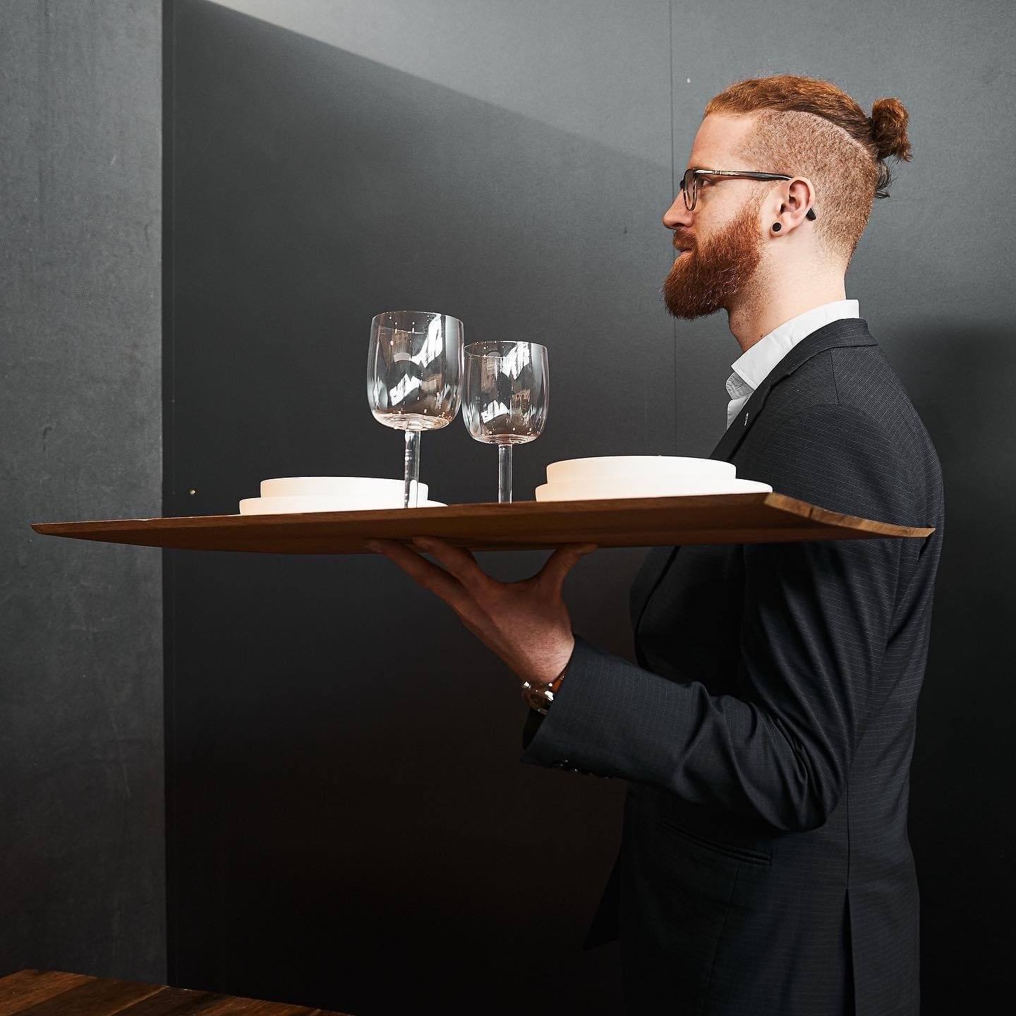 Eine Person, die ein Serviertablett aus Altholz mit Geschirr darauf auf einer Hand trägt